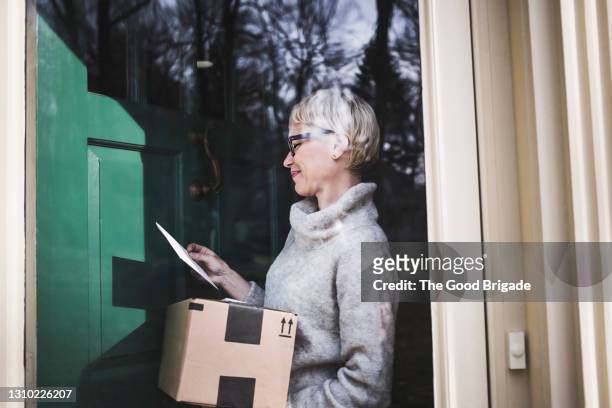 woman receiving package at front door of home - package delivery stock-fotos und bilder