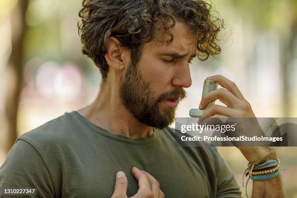 een man gebruikt een astma-inhalator in public park. - asthma stockfoto's en -beelden