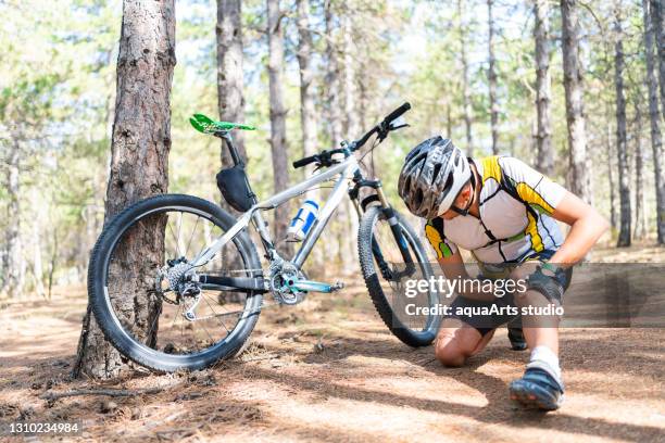 a male mountain bicycle rider injured while out on a bike ride in nature - injured knee stock pictures, royalty-free photos & images