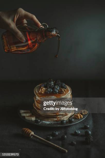 pancake con mirtilli, more, banane, noci e sciroppo di acero su fondo scuro - sciroppo stock pictures, royalty-free photos & images