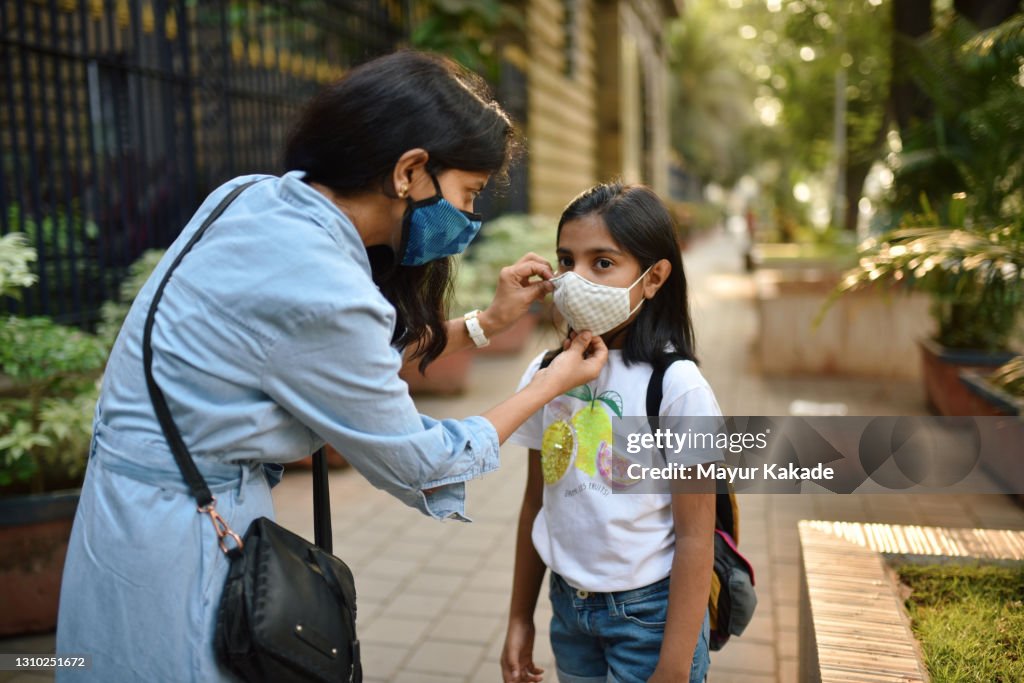 Mother putting protective face mask on her daughter's face