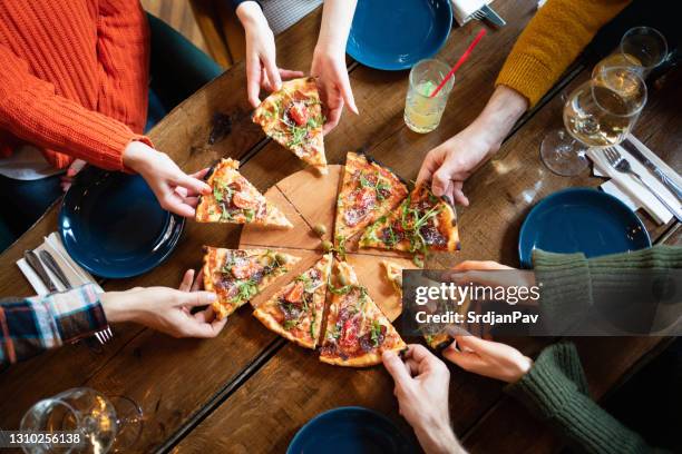 primo-up di persone mani che prendono fette di pizza dalla tavola di legno - bar overhead foto e immagini stock