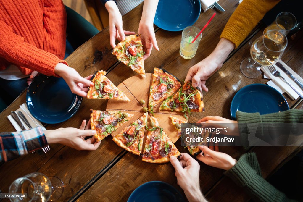 Close-up of people hands taking slices of pizza from the wooden board