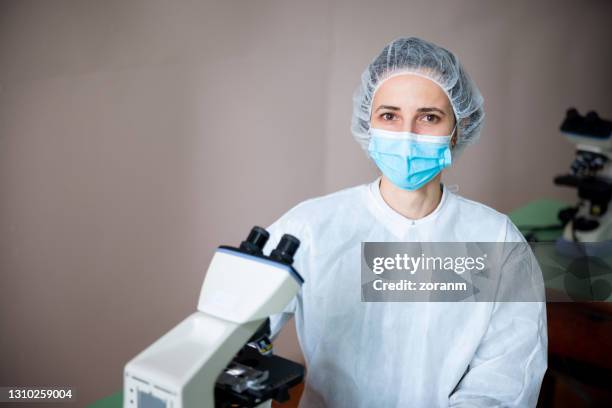 female scientist in protective headwear and mask working in microscopy lab - microbiologist stock pictures, royalty-free photos & images
