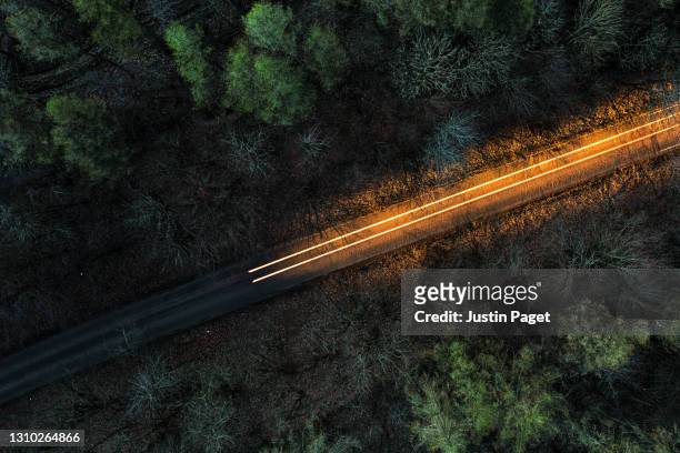drone view above a road through a forest at night - straßenverkehr stock-fotos und bilder