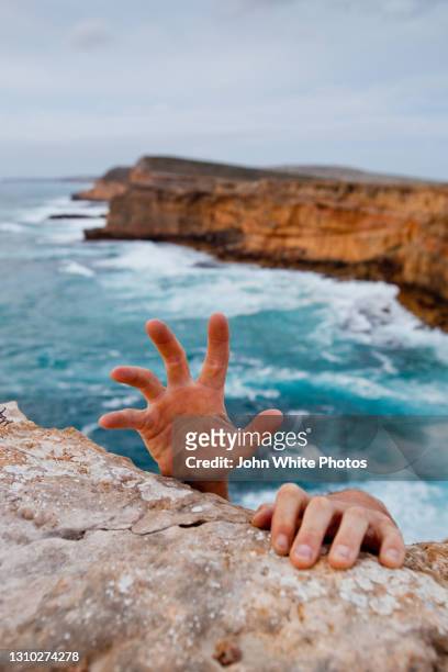 hands reaching up to grip a cliff. dangerous ocean in the background. - cliff stock pictures, royalty-free photos & images