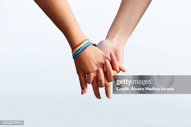 hands of unrecognizable lesbian female couple with lgbt rainbow bracelet - gay flag stockfoto's en -beelden