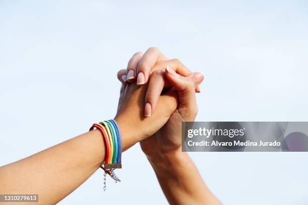 hands of unrecognizable lesbian female couple with lgbt rainbow bracelet - bracelet fotografías e imágenes de stock