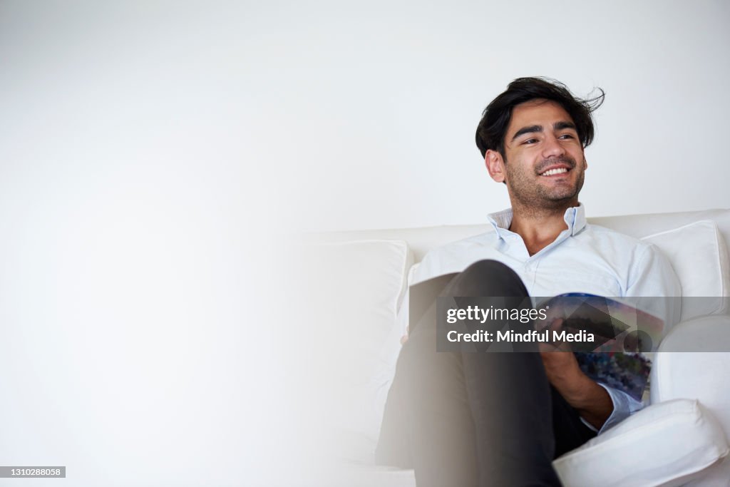 Joven sonriente sosteniendo revista mientras estaba sentado en el sofá