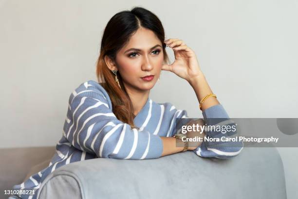 contemplating young asian woman sitting on a sofa - porträt frau blick in ferne stock-fotos und bilder