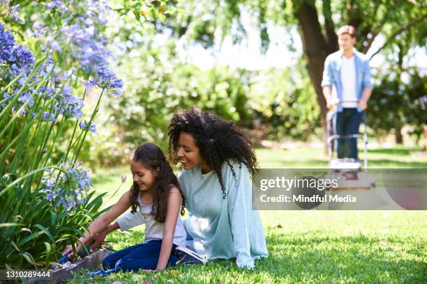 mother and daughter planting together in garden while father is mowing the lawn in the background - cutting grass stock pictures, royalty-free photos & images