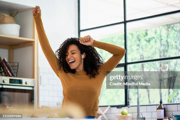 smiling woman listening music and dancing in kitchen - danser stock pictures, royalty-free photos & images