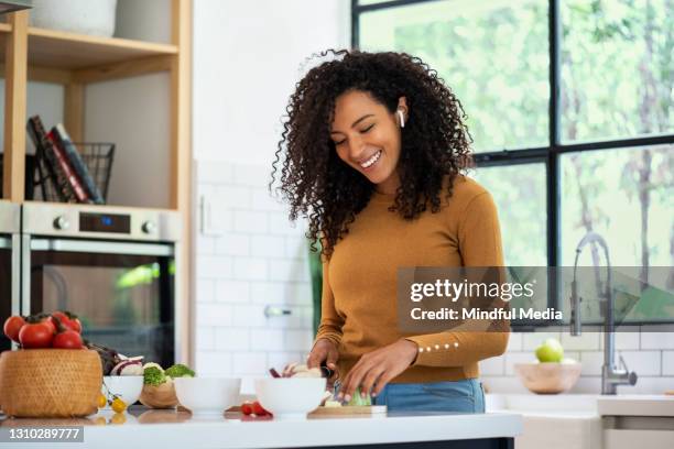 femme de sourire écoutant la musique et coupant des légumes dans la cuisine - in ear headphones photos et images de collection