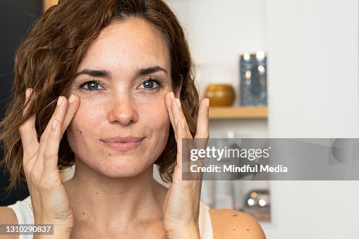Primer plano de la mujer aplicando crema a sus cheeckbones usando ambas manos Primer plano de la mujer aplicando crema a sus cheeckbones usando ambas manos