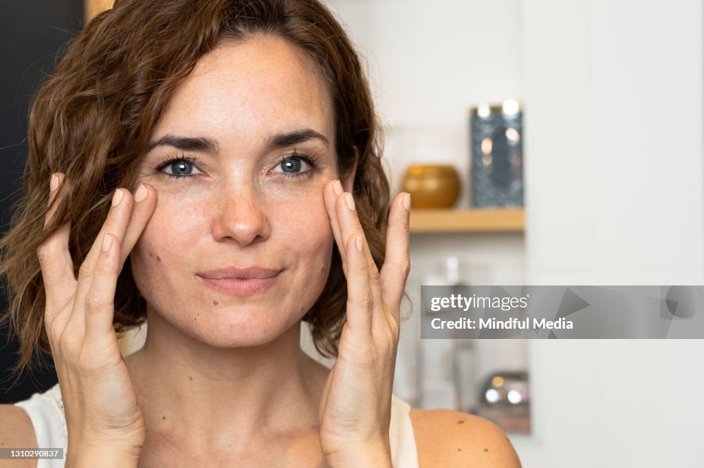 Close-up of woman applying cream to her cheeckbones using both hands