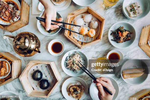 flat lay of assorted traditional chinese dim sum in bamboo steamer with a variety of appetitzers freshly served on table with two people enjoying meal and eating with chopsticks in restaurant. chinese cuisine and food culture. yumcha. eating out lifestyle - dining ストックフォトと画像