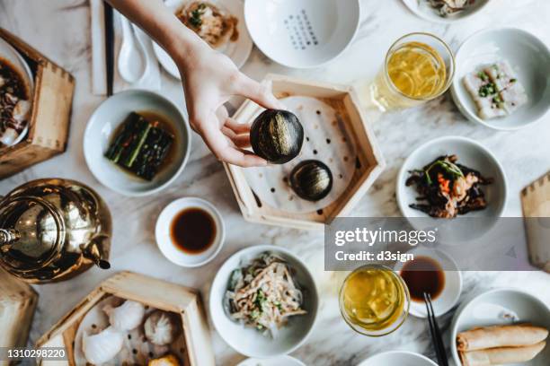 flat lay of assorted traditional chinese dim sum in bamboo steamer with a variety of appetitzers freshly served on table with a woman enjoying meal and holding a steamed bun in restaurant. chinese cuisine and food culture. yumcha. eating out lifestyle - fusion food stock pictures, royalty-free photos & images