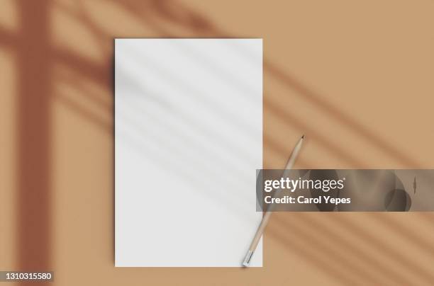 blank paper and pencil in brown background with window shadow - paper clip stockfoto's en -beelden