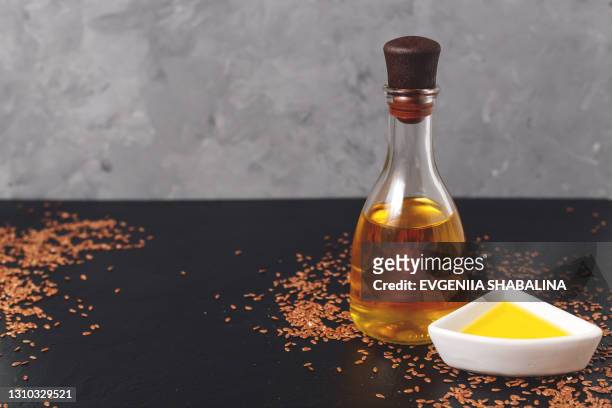 flax seeds in white bowl and a glass bottle of linseed oil on a dark and grey background - flax seed fotografías e imágenes de stock