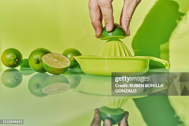 front view of a hand squeezing a half green citric lime and a juicer to squeeze them with reflection on the glass mirror of a table on a green backgrounds. horizontal photo - juicing stock pictures, royalty-free photos & images