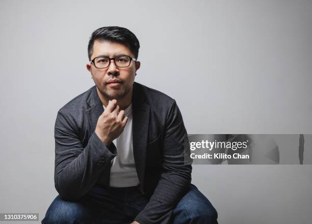 studio shot of an asian man with a serious face sitting with hand on chin - asian man seated stockfoto's en -beelden