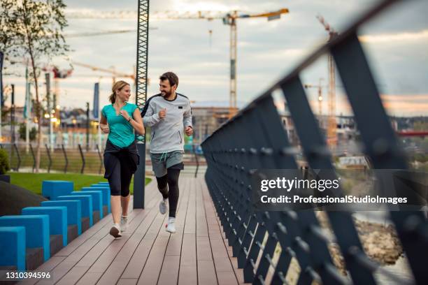 einfach weiterlaufen! young sportsman und seine teamkollegin laufen und joggen auf der brücke in der dämmerung. gesundheitsaktivitäten. - riverbank stock-fotos und bilder