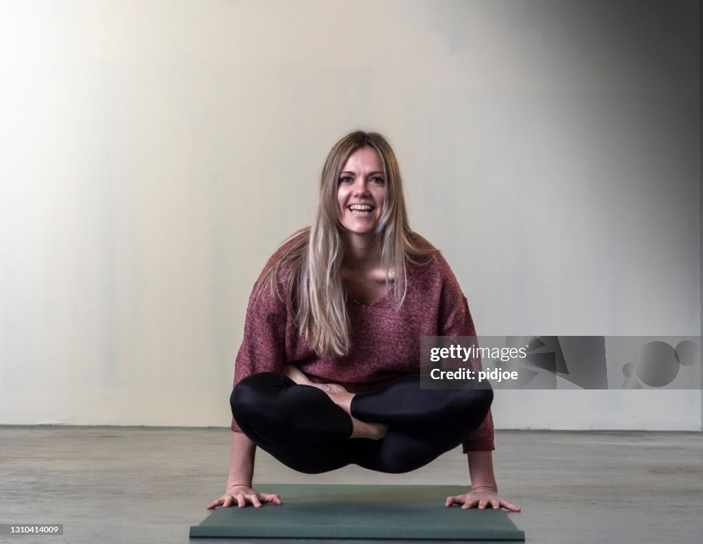Woman doing yoga at gym in floating lotus position on hands, scales pose