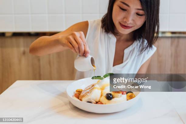 young woman pouring maple syrup on pancake at cafe - maple syrup pancakes stockfoto's en -beelden