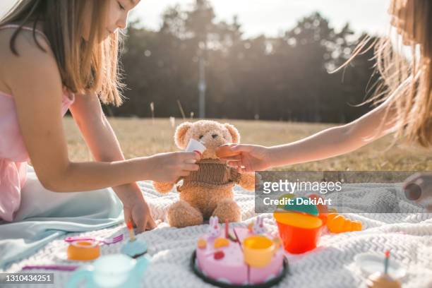 sisters feeding their teddy bear on a picnic - teddy bear stock pictures, royalty-free photos & images