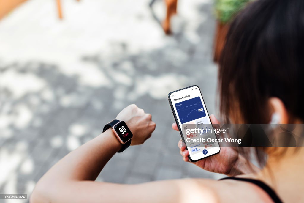 Young Woman Using Fitness Tracker App On Smart Watch And Smartphone