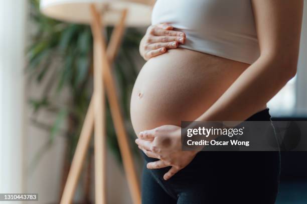 midsection of pregnant woman holding her belly - femme main ventre photos et images de collection