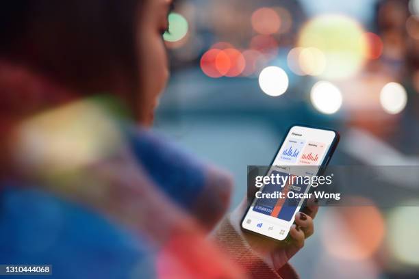 young woman accessing mobile banking with smartphone while walking on urban city street - über die schulter stock-fotos und bilder