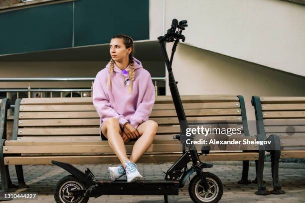 portrait of woman who using electric kick scooter. push scooter concept outdoors the street. person with glasses and wireless headphones is sitting and relaxing on bench near electric scooter. - girl riding scooter stock pictures, royalty-free photos & images