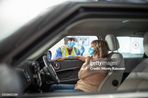 male nurse in hi-vis vaccinating woman in car in drive-in covid vaccination centre - drive through mask stock pictures, royalty-free photos & images