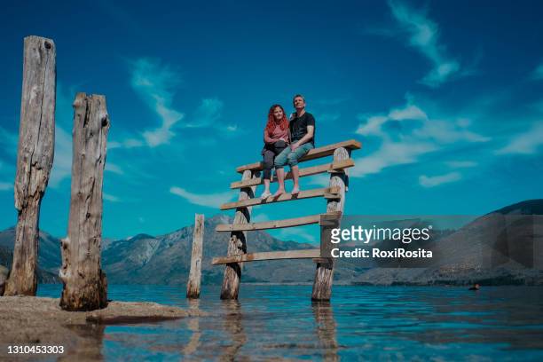 couple sitting on a ladder at lake epuyen in patagonia argentina. sunny day with clouds - chubut province ストックフォトと画像