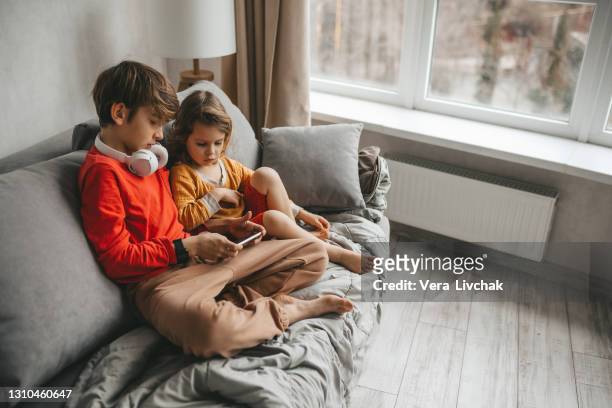 two children boy and girl using mobile phone on sofa at home. - baby monitor stock-fotos und bilder