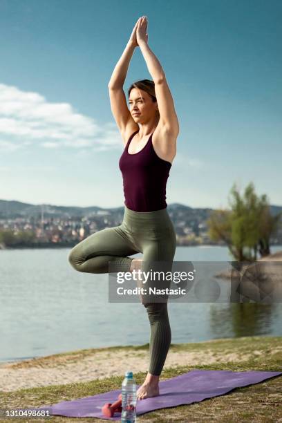 young adult woman practicing yoga near a river on sunny day - sun salutation stock pictures, royalty-free photos & images