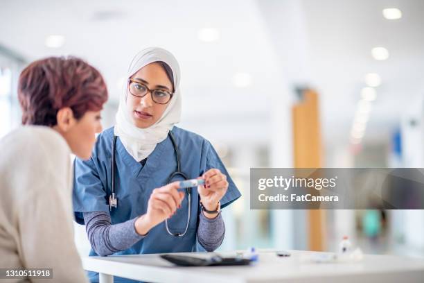 female muslim doctor showing a diabetic patient an insulin pen - hijab stock pictures, royalty-free photos & images
