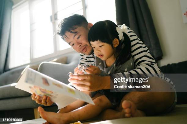 quality times father enjoyment time reading abook with daughter at home weekend activitiy - asian family stockfoto's en -beelden