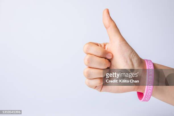 thumbs up hand with "covid-19 vaccinated" rubber wristband - rubber bracelet stock pictures, royalty-free photos & images