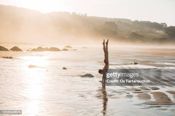 silhouette of a girl doing a handstand in an empty beach at sunset. side view. - handstand beach stock pictures, royalty-free photos & images