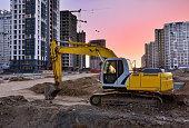 Excavator during earthmoving work at construction site on sunset background
