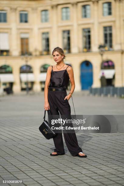 Xenia Adonts wears earrings, a golden necklace, a black silky off-shoulder tank top from Attire The Studio, a Loewe black leather belt with golden...