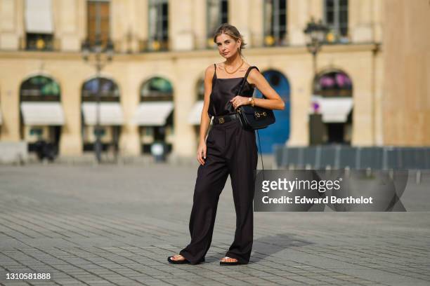 Xenia Adonts wears earrings, a golden necklace, a black silky off-shoulder tank top from Attire The Studio, a Loewe black leather belt with golden...