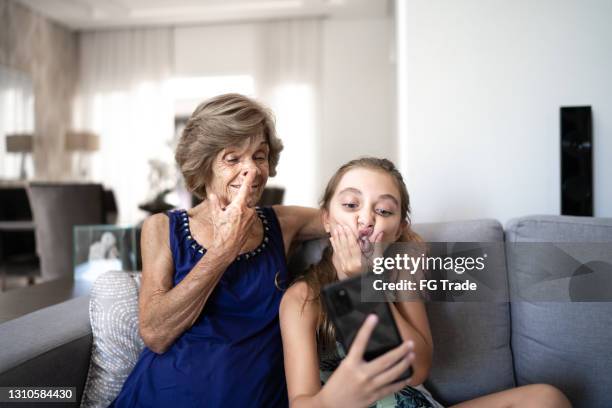 fille faisant un visage prenant le selfie avec la grand-mère à la maison - mamie grimace photos et images de collection