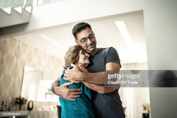 hijo abrazando a madre en casa - hijo fotografías e imágenes de stock