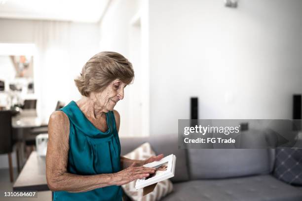 sad senior woman looking at a photo frame at home - widow pension stock pictures, royalty-free photos & images