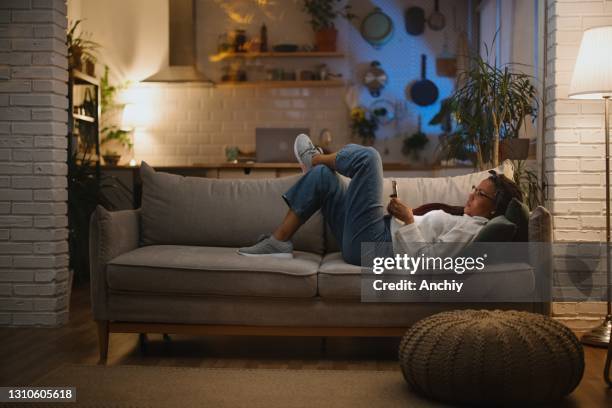 donna annoiata sdraiata nel divano a tarda notte mentre usa il suo smartphone - donna poltrona foto e immagini stock
