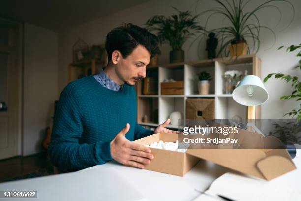 young man feeling disappointed after he unpacking a parcel with the wrong order at home - disappointment gift stock pictures, royalty-free photos & images