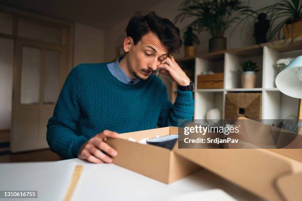 kaukasier mann fühlt sich enttäuscht, nachdem er ein paket mit der falschen bestellung zu hause auspacken - enttäuscht stock-fotos und bilder